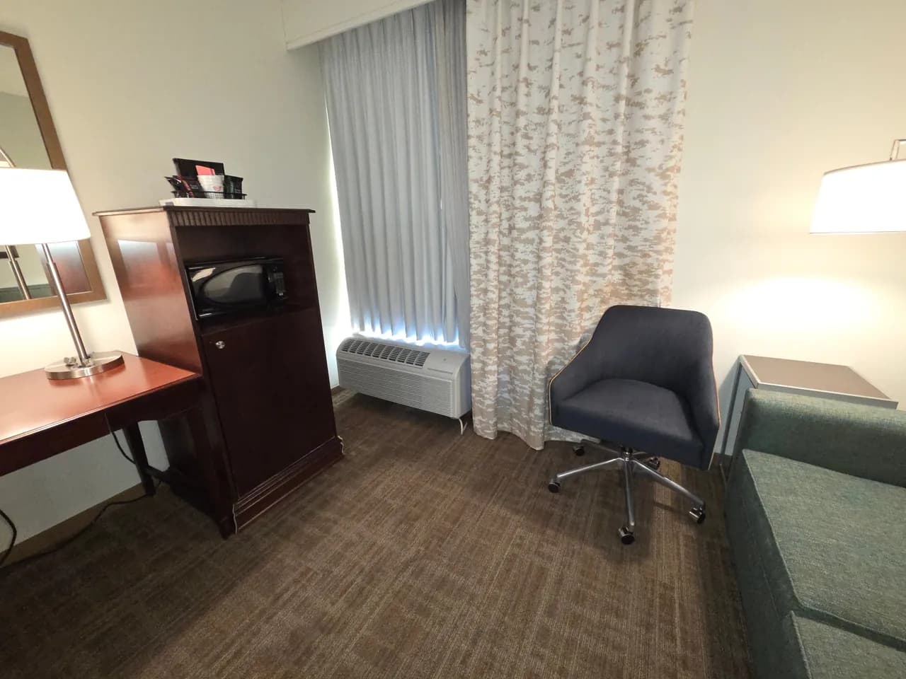 Hotel room seating area with a desk, chair, lamps and microwave cabinet beside the window